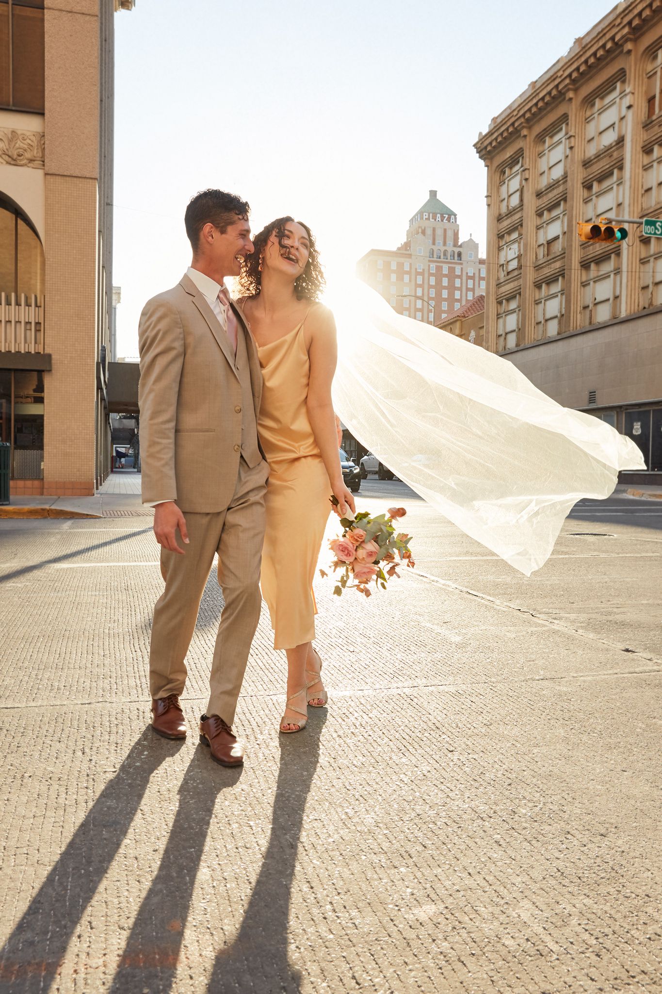 Flowing white veil catches sunlight against historic brick building backdrop.