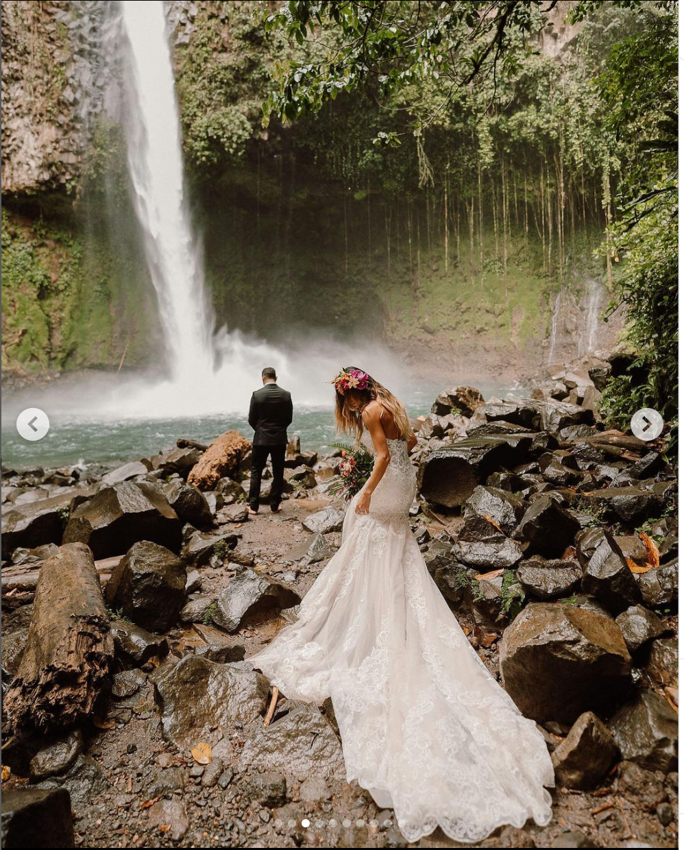 Wedding couple standing on rocky shore near majestic waterfall.