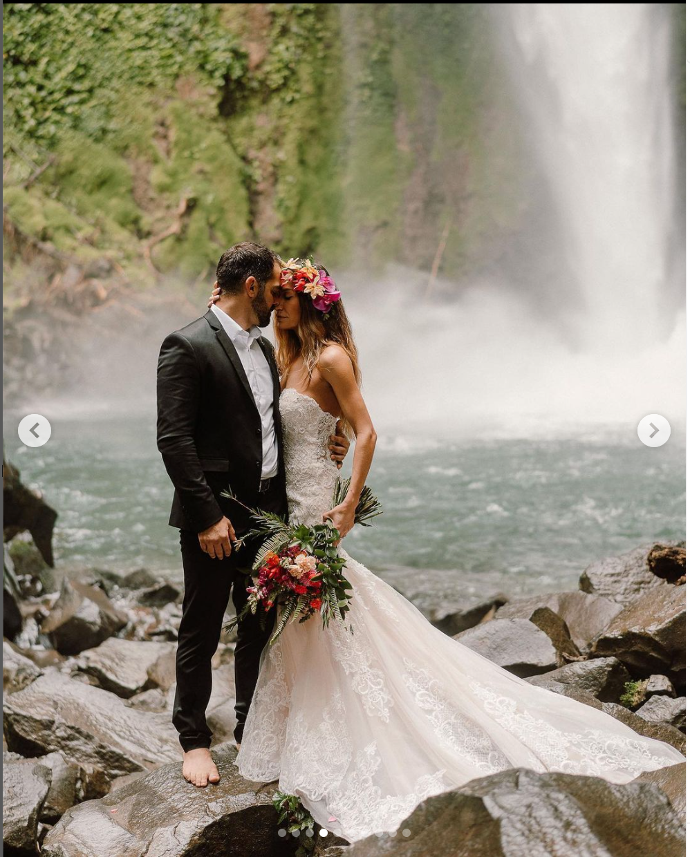 Wedding photoshoot at base of waterfall with couple on rocky terrain.