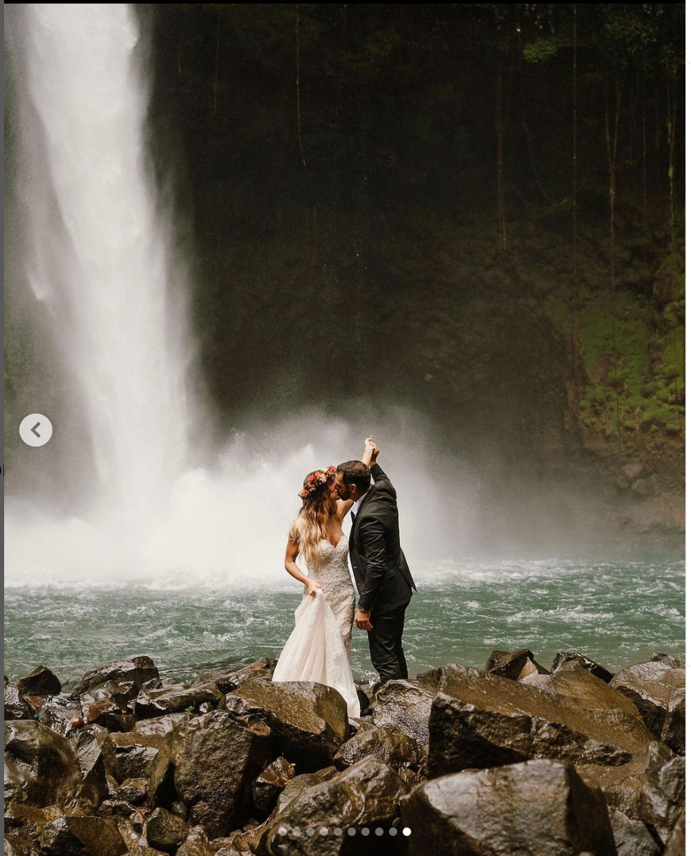 Couple embracing on rocky outcrop with waterfall mist in background.