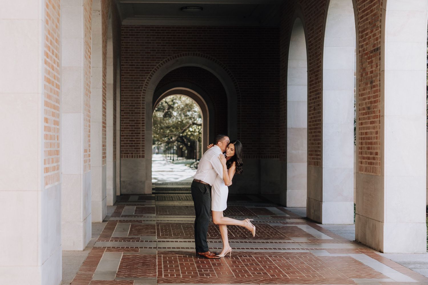 A romantic embrace in a brick archway corridor with sunlight streaming through.