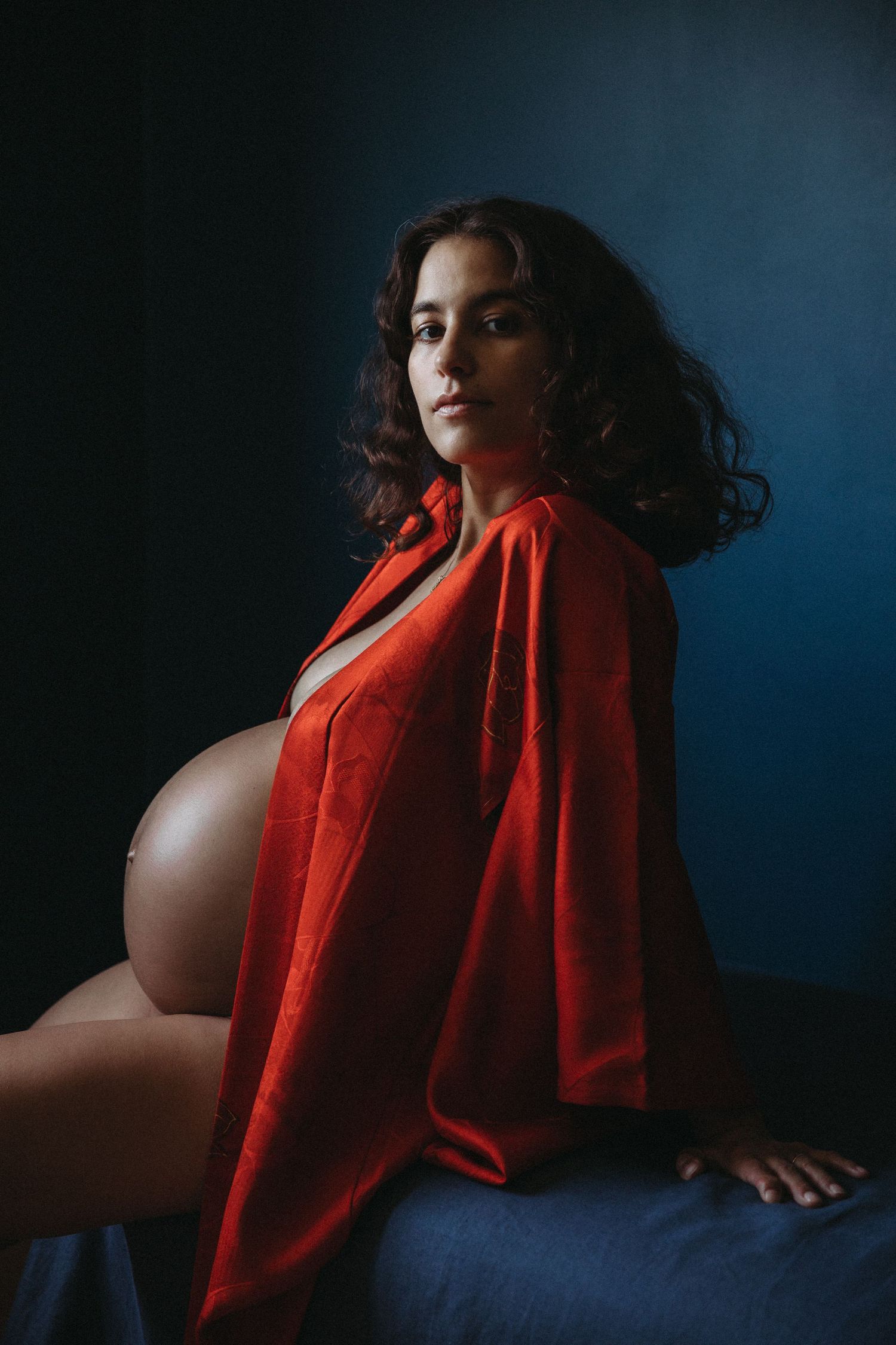 woman in red robe poses for portrait with pregnant belly on display for pregnancy photographer london sarah stirk