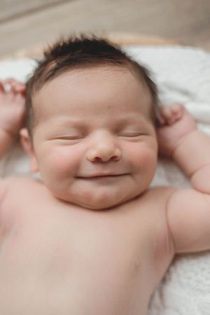 Smiling sleeping newborn baby with dark hair resting on white blanket indoors.