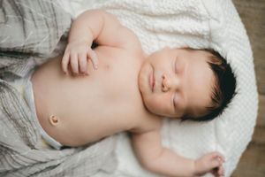 Sleeping newborn baby with dark hair resting on white blanket with gray wrap.