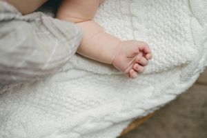 Close-up of a newborn baby's tiny hand resting on a soft white knit blanket.