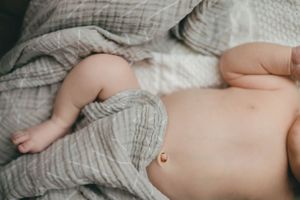 Peaceful newborn baby lying on grey muslin blankets showing tiny belly and umbilical cord.