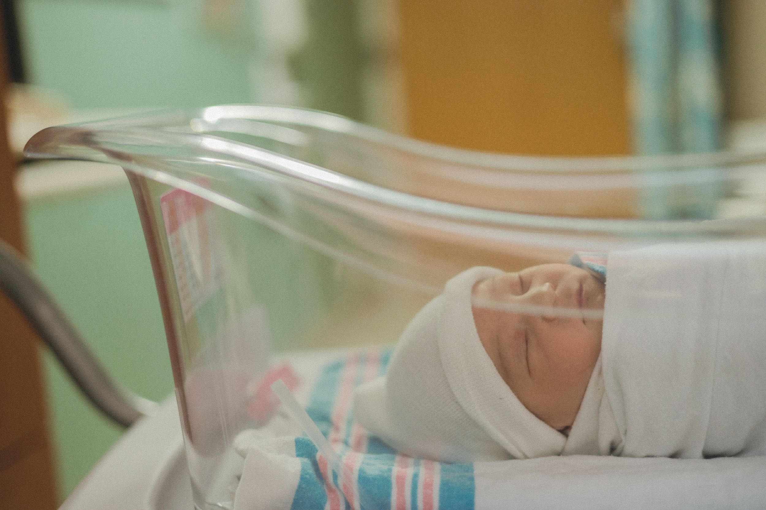 Swaddled newborn baby sleeping peacefully in hospital bassinet after birth.