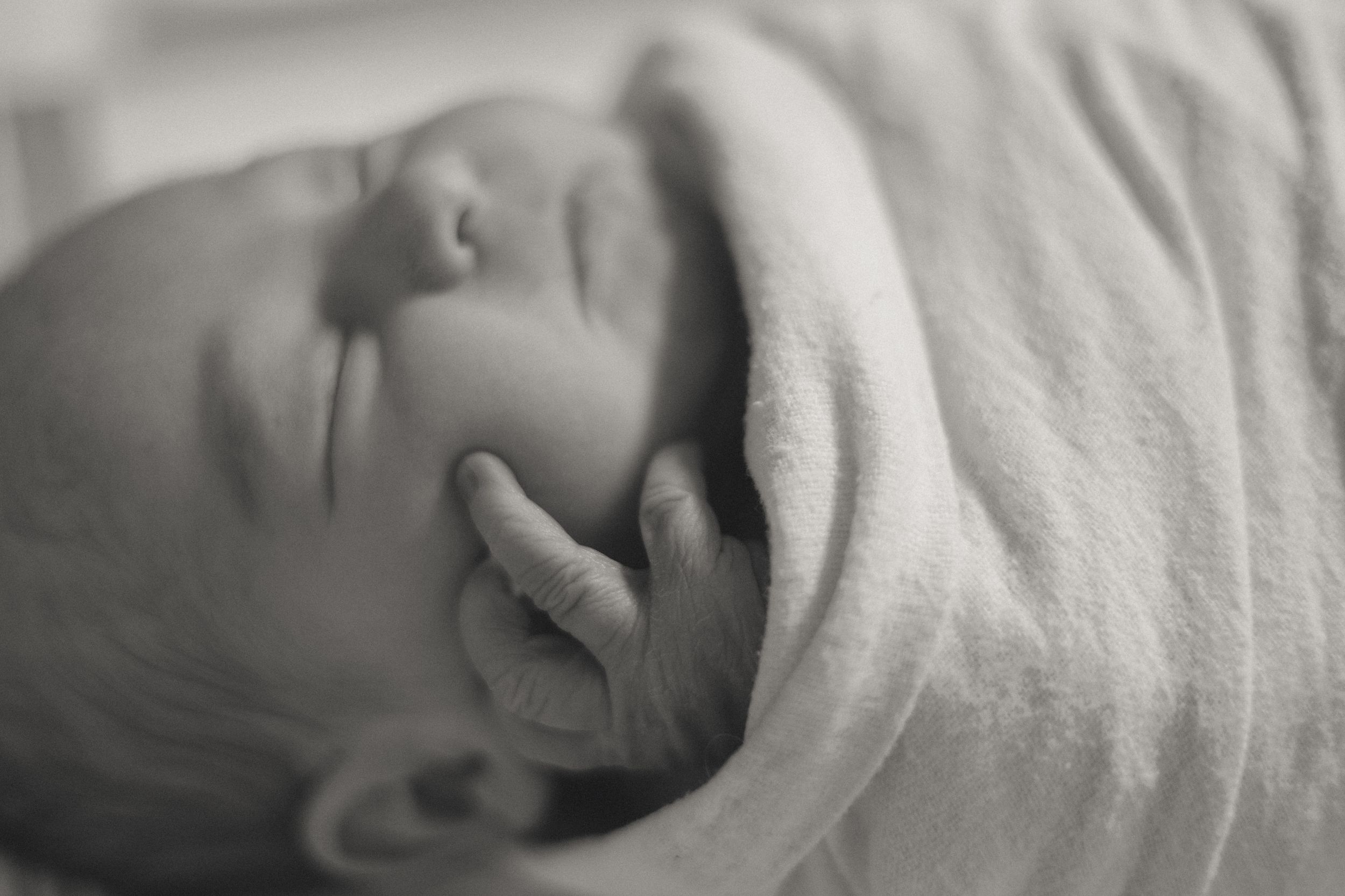Black and white close-up of a sleeping newborn baby swaddled in a soft white blanket.