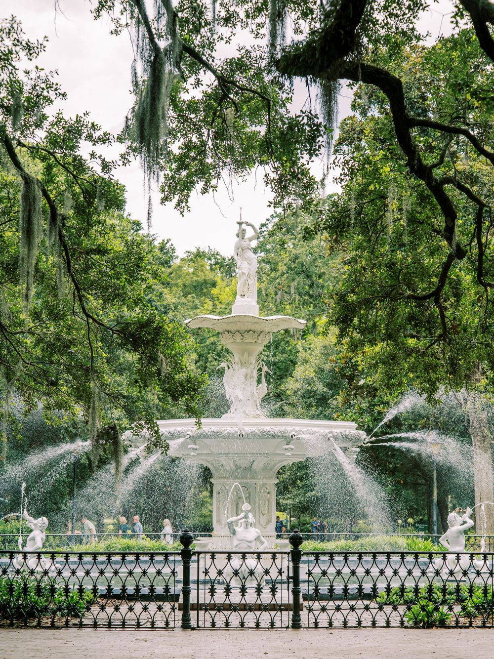 Ornate white fountain spraying water in a formal garden with Spanish moss draped trees.
