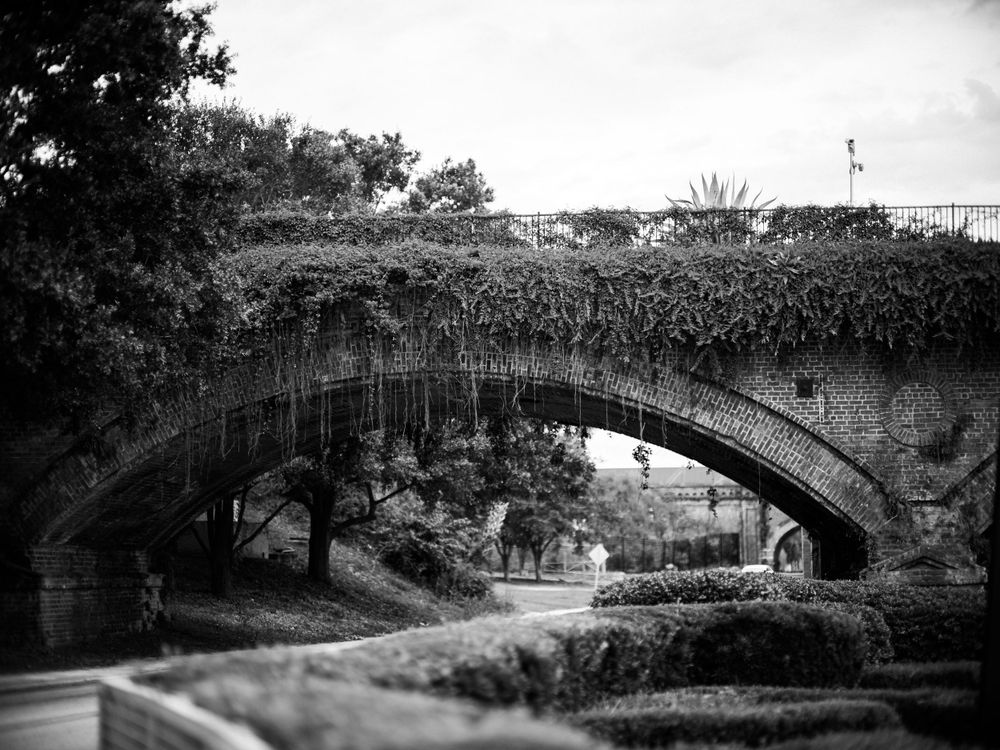 Black and white photograph of an old stone bridge arch over a path.
