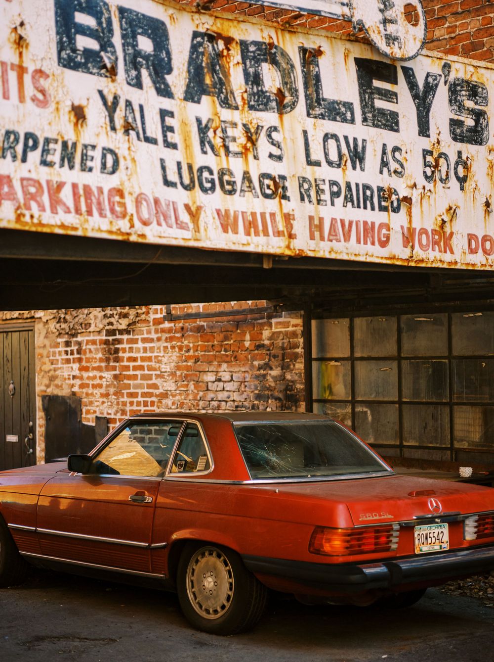 Vintage red Mercedes parked under rustic sign for Bradley's locksmith and key repair service.