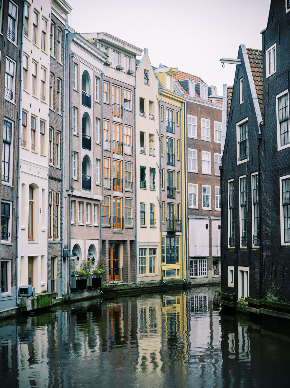 Colorful historic canal houses with traditional Dutch architecture reflect in Amsterdam's waterways.