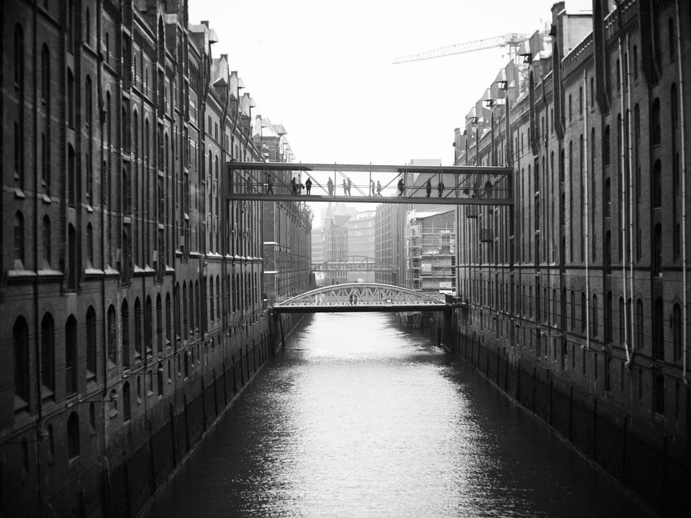 Black and white photograph of a canal in Hamburg's historic warehouse district with connecting bridges.