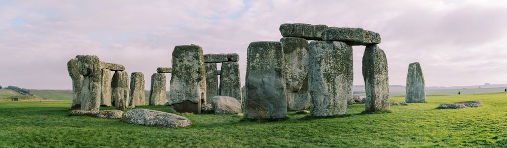 Ancient Stonehenge monument stands mysteriously on green grassland under cloudy skies.