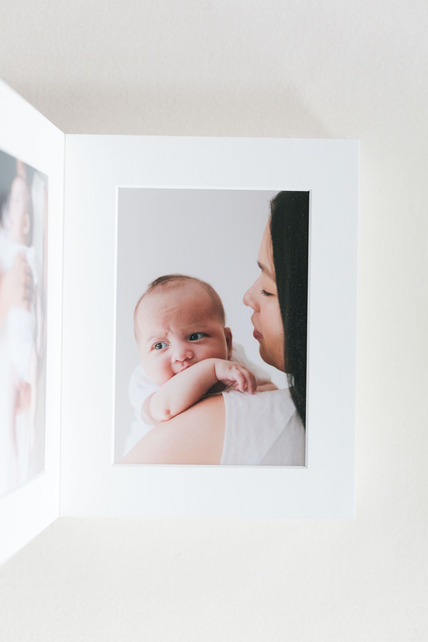 an overhead view of an open matted album showcasing a photo of a mom holding her baby against a white background