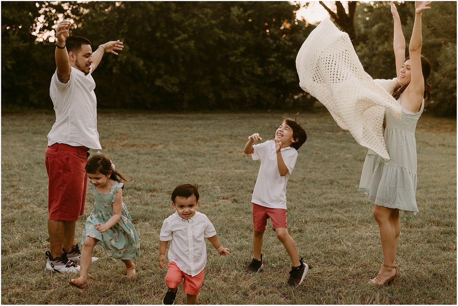 Family playing and jumping together outdoors in a playful moment at sunset.
