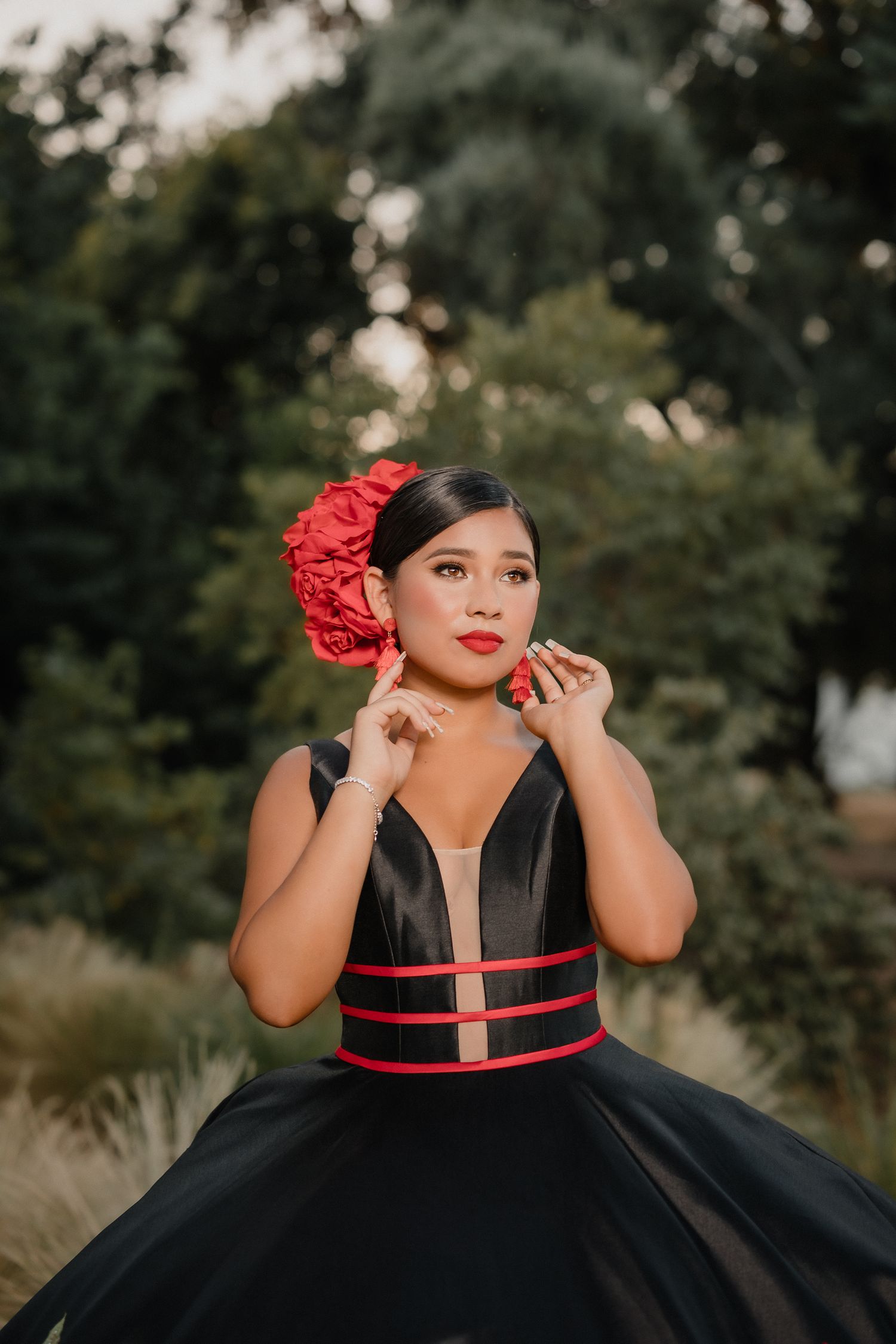 A dramatic black ball gown with red accents photographed outdoors with a bokeh background.