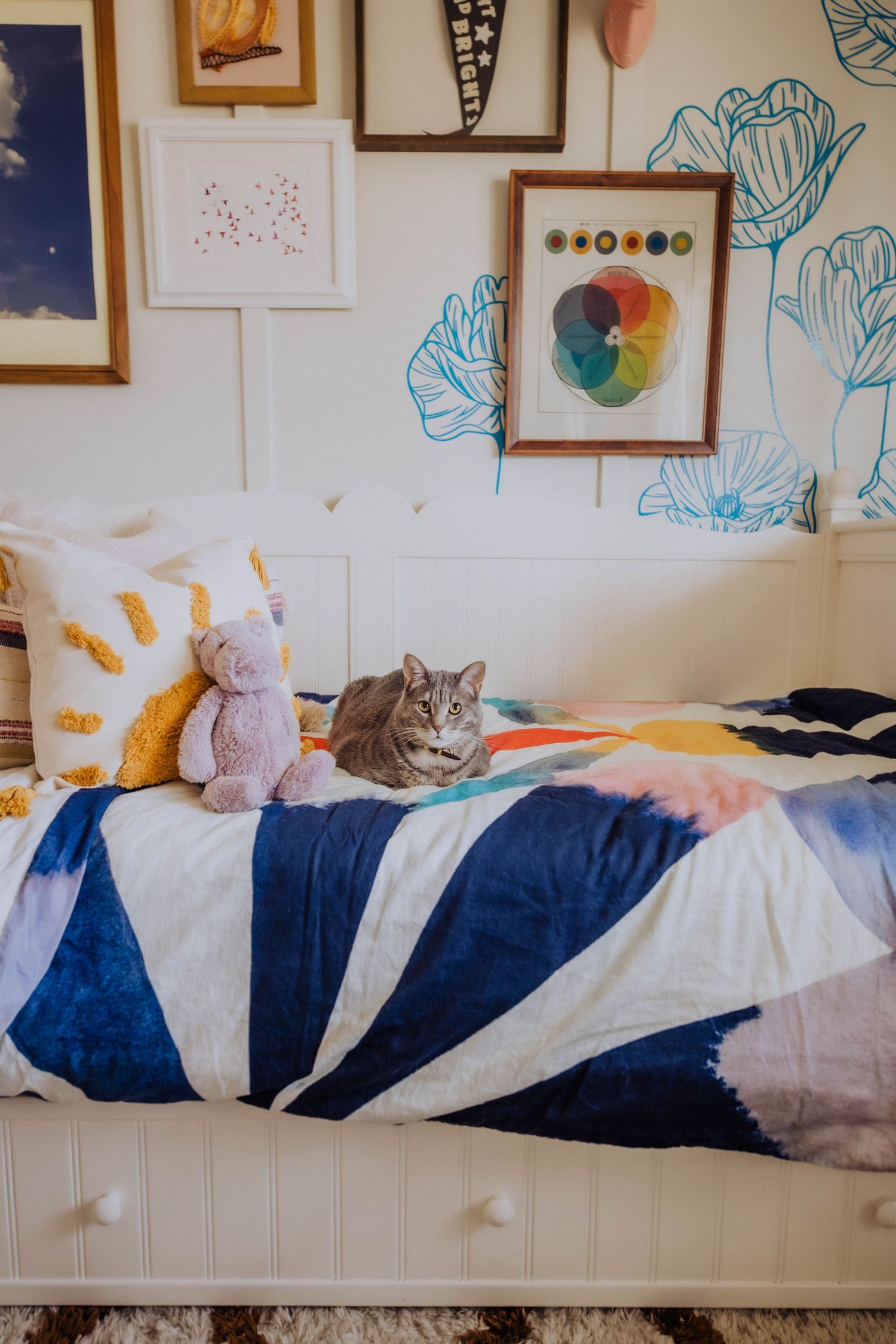 Bed with blue and white striped bedding and plush toys against floral wall art.