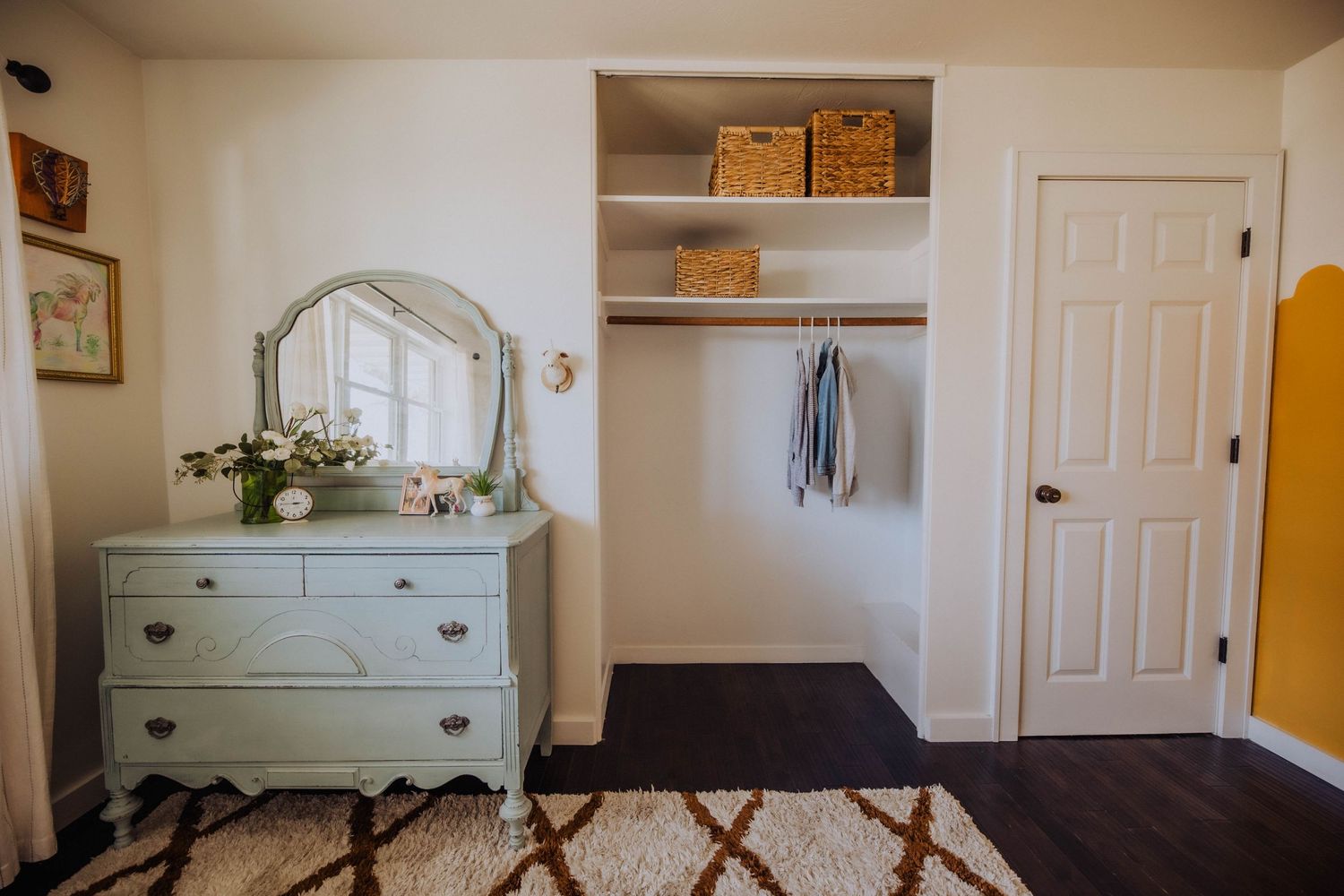 Modern nursery with geometric rug, vintage dresser, and floating shelves displaying children's books.