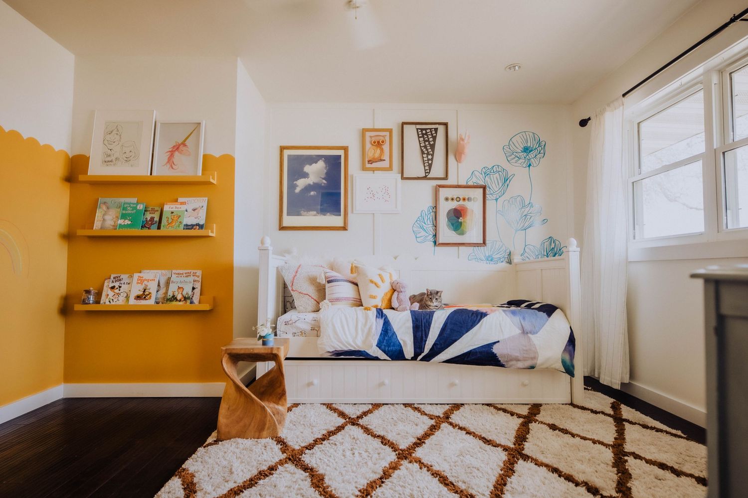 Yellow and white nursery with wall art, floating bookshelves, and a patterned area rug.
