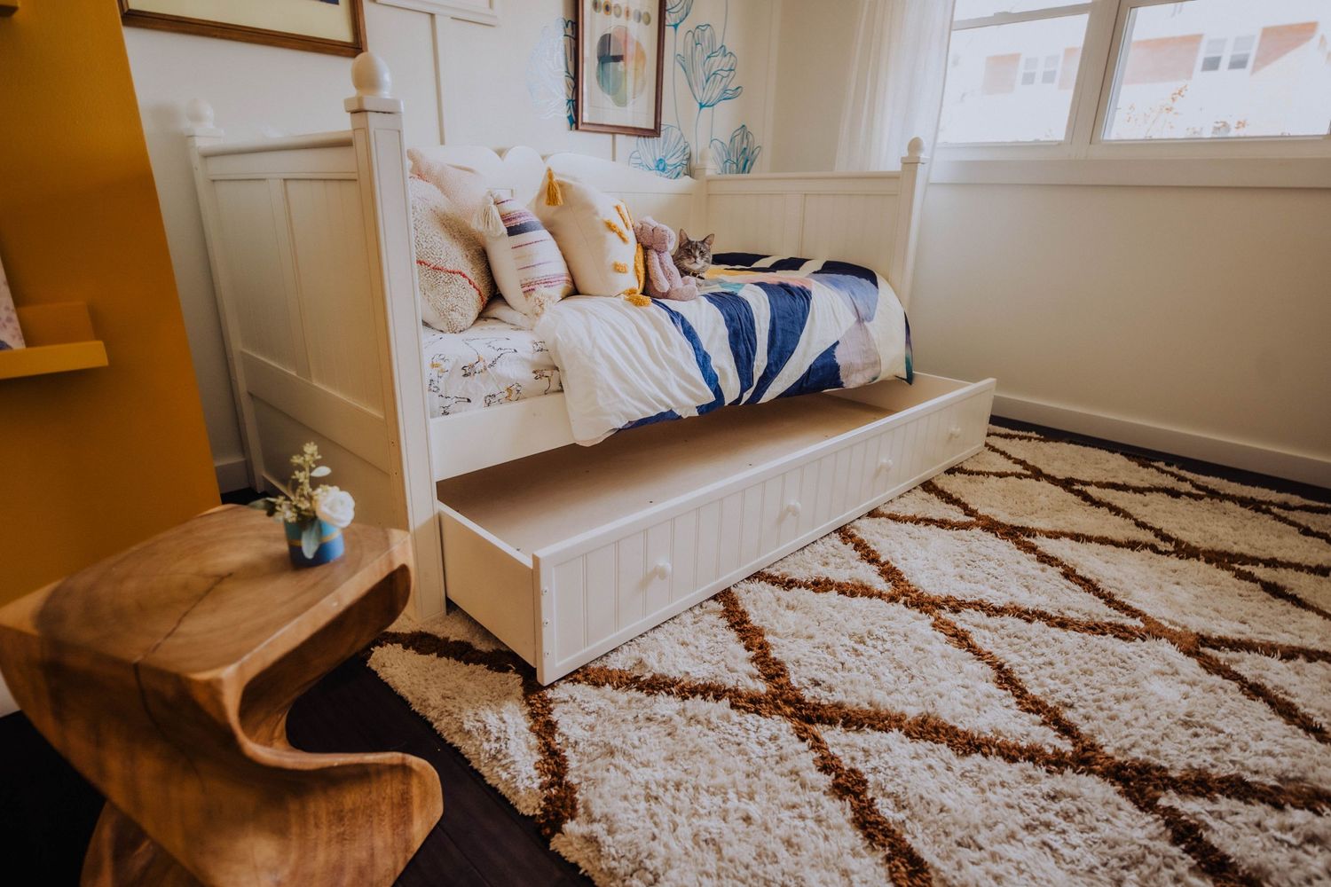 Bright nursery room featuring blue wall decals, white furniture, and a geometric brown and white rug.