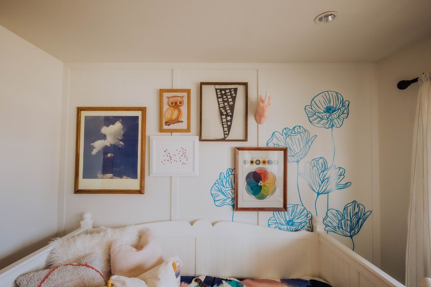 Nursery wall decorated with turquoise floral decals and framed artwork in various styles.