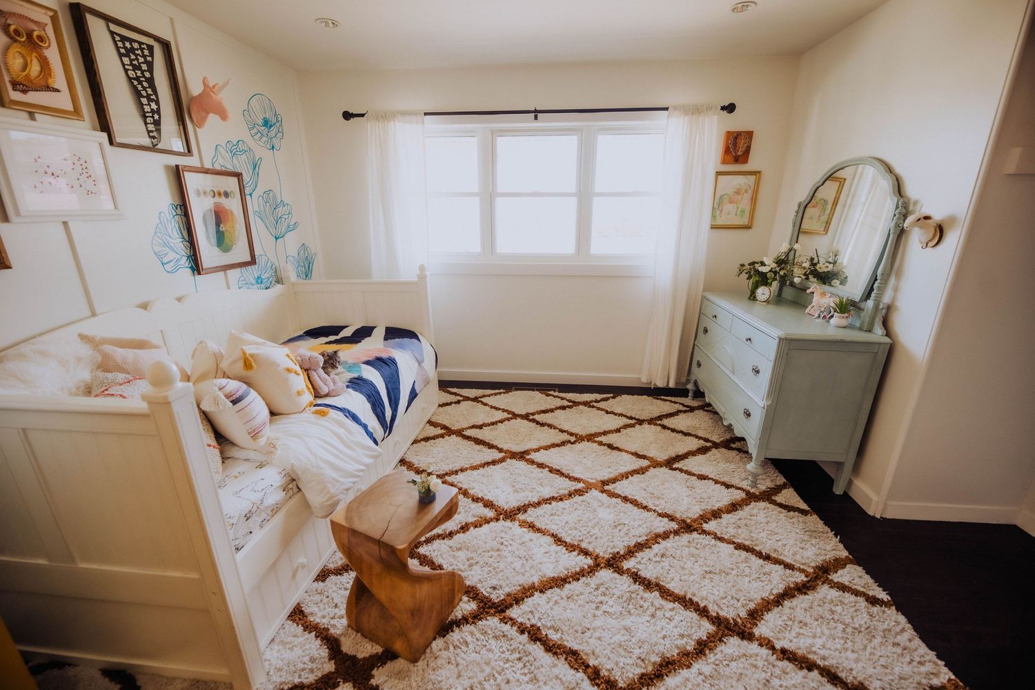 Wide view of a nursery with geometric rug, mint green dresser, and decorative wall art.