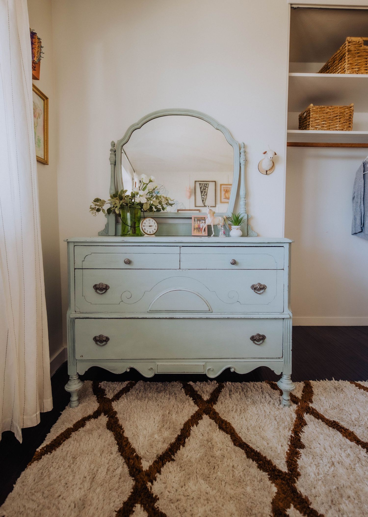 Vintage-style mint green dresser with mirror against white wall, with geometric rug below.