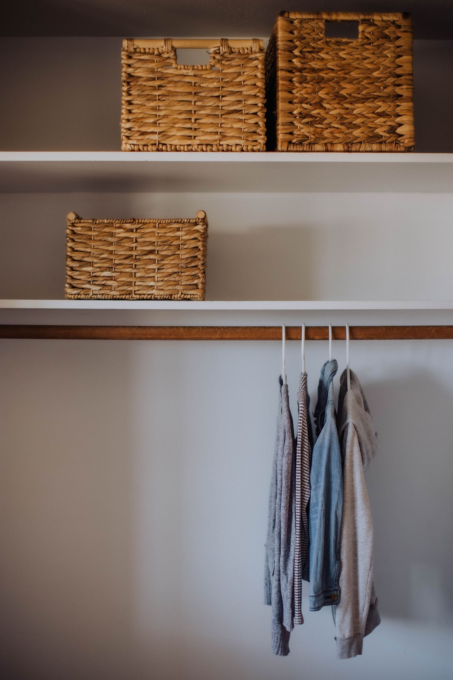 White shelving unit with woven storage baskets and hanging clothes.