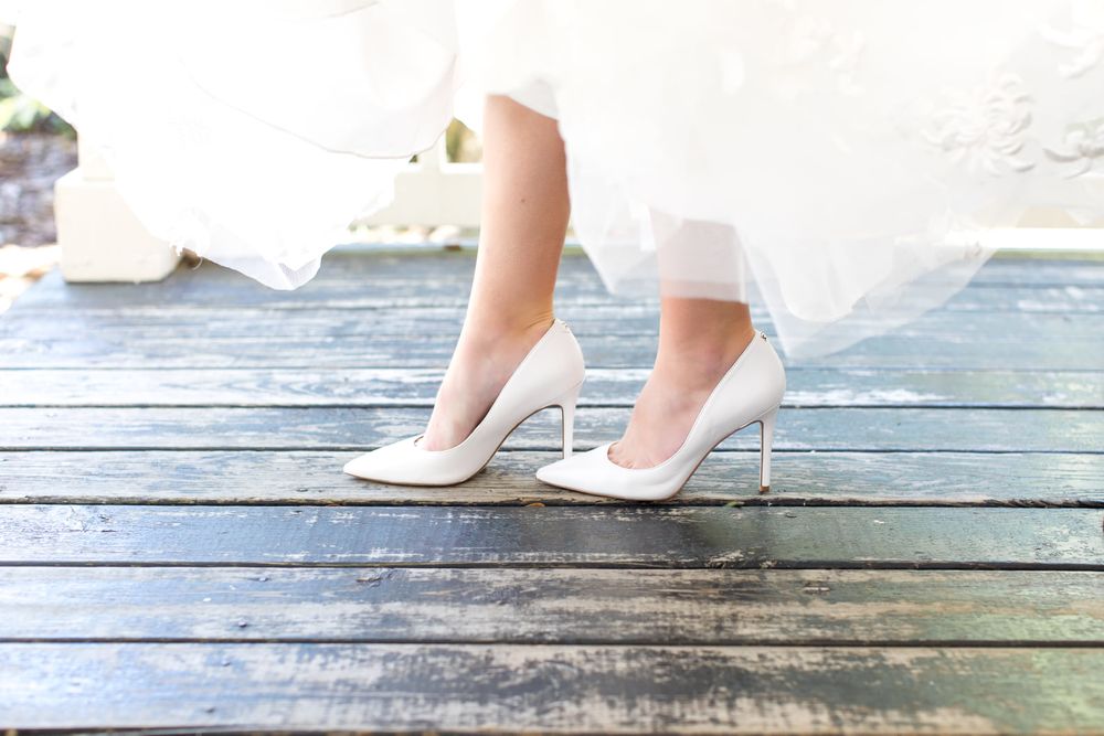 White high heeled wedding shoes on a weathered wooden deck or boardwalk.