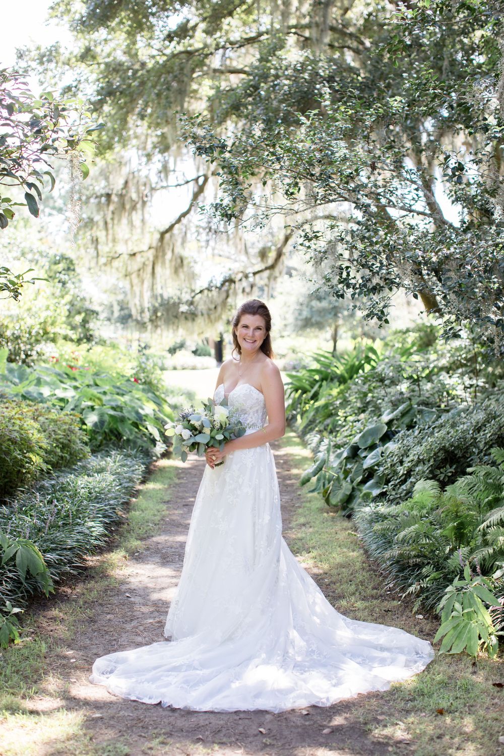 Wedding dress photographed on garden path with Spanish moss hanging from trees.