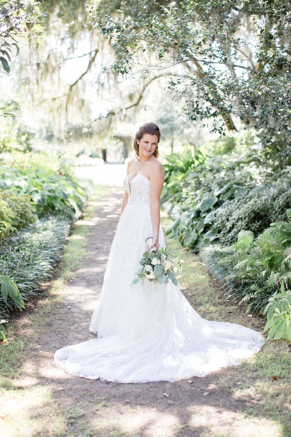 Bridal portrait on garden path surrounded by lush greenery and Spanish moss.