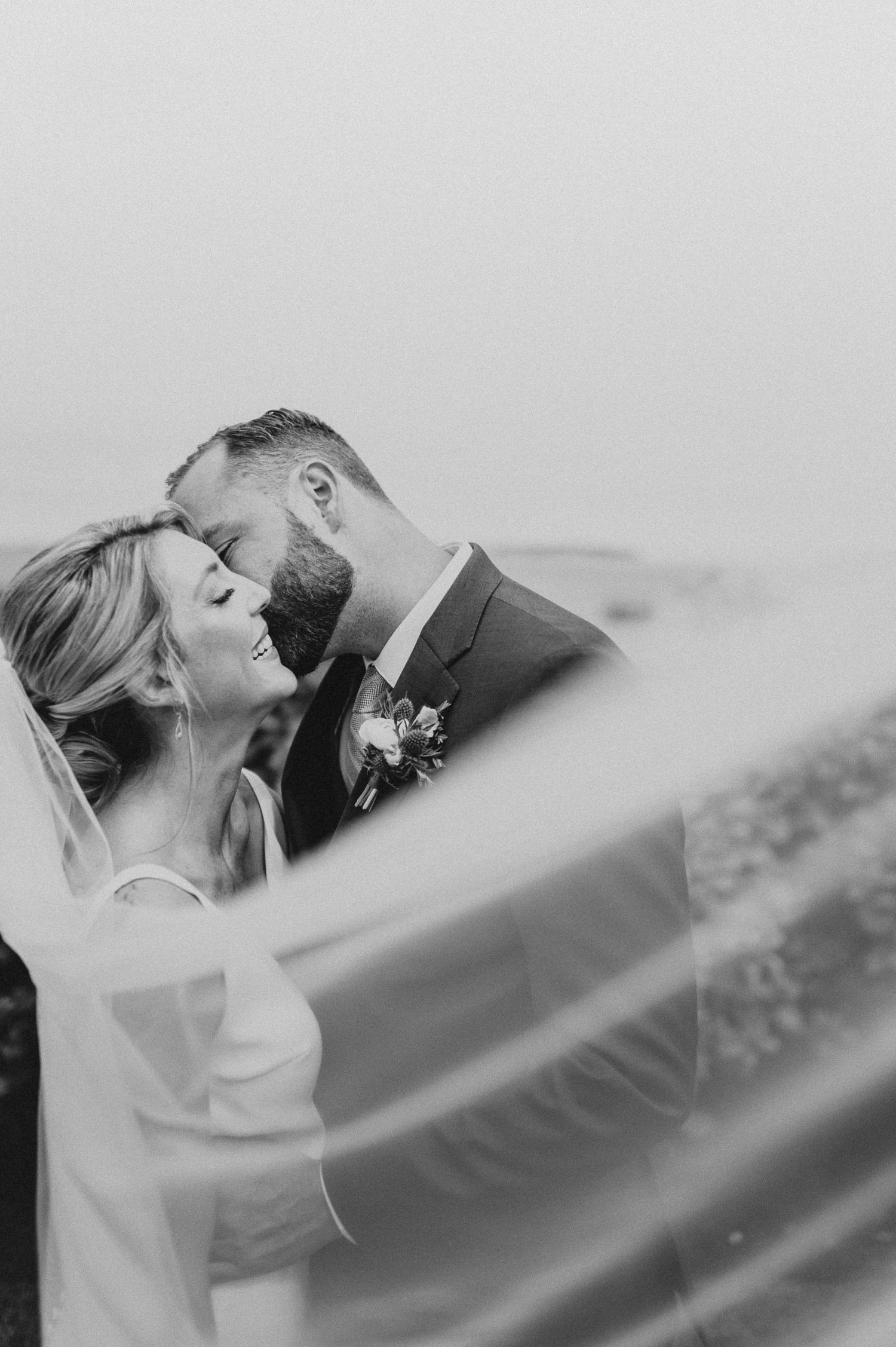 Artistic black and white wedding portrait with flowing veil creating dramatic effect.
