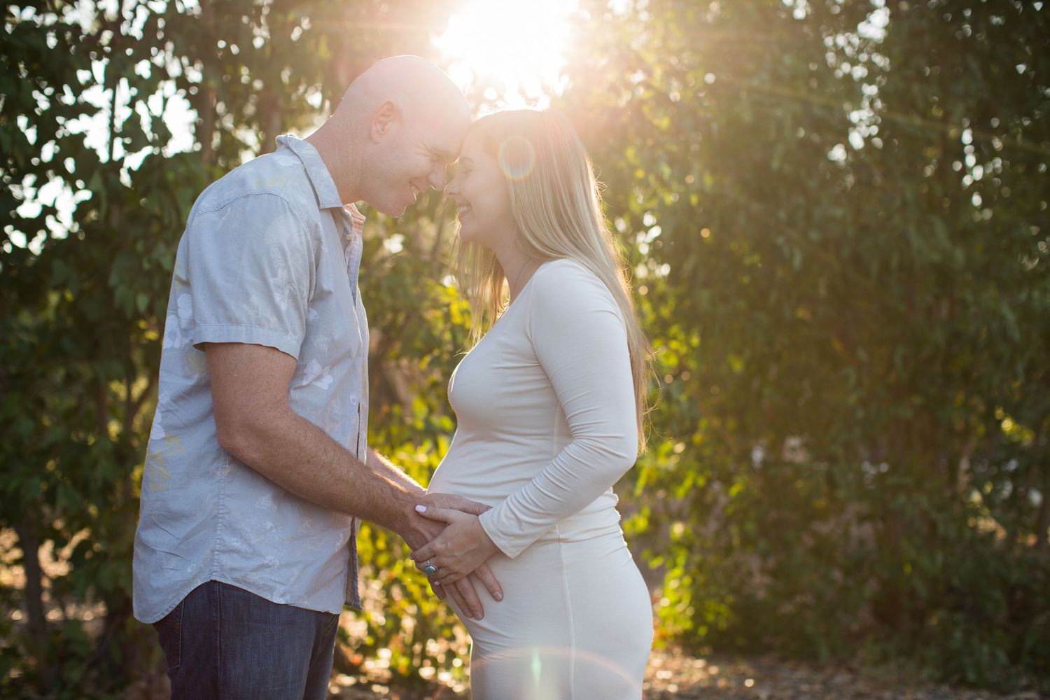 Backlit silhouette of an expectant couple sharing an intimate moment in golden sunset light.