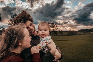 Family photo taken near Winchester Virginia, dad holding baby looking at camera while mom looks at baby, dramatic sky