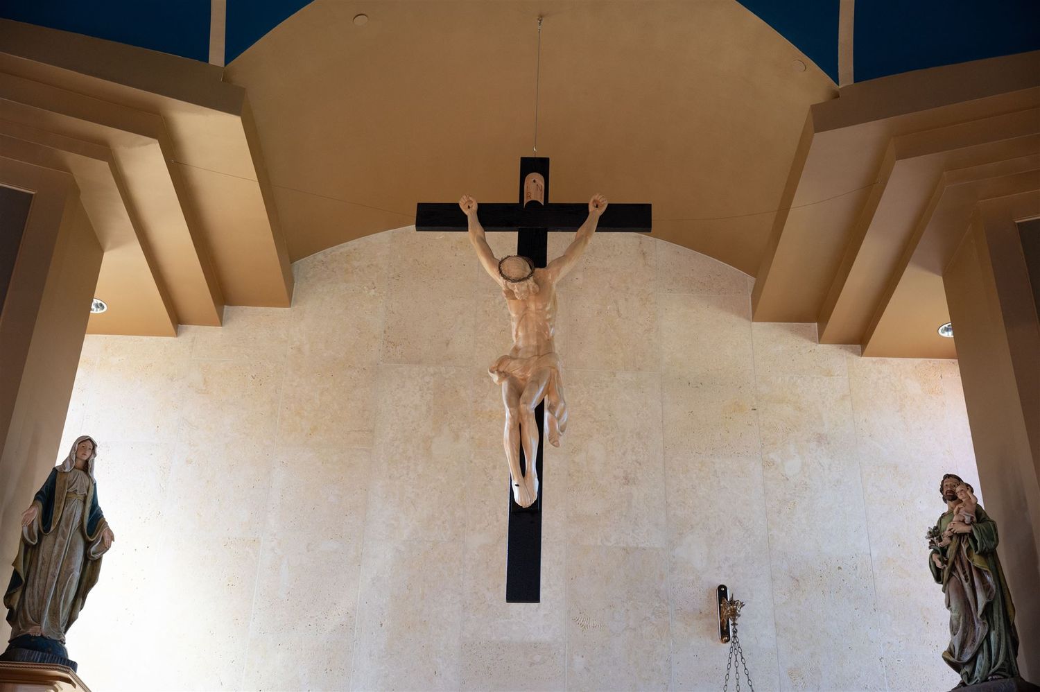 Religious crucifix mounted on white church wall with decorative architectural elements.