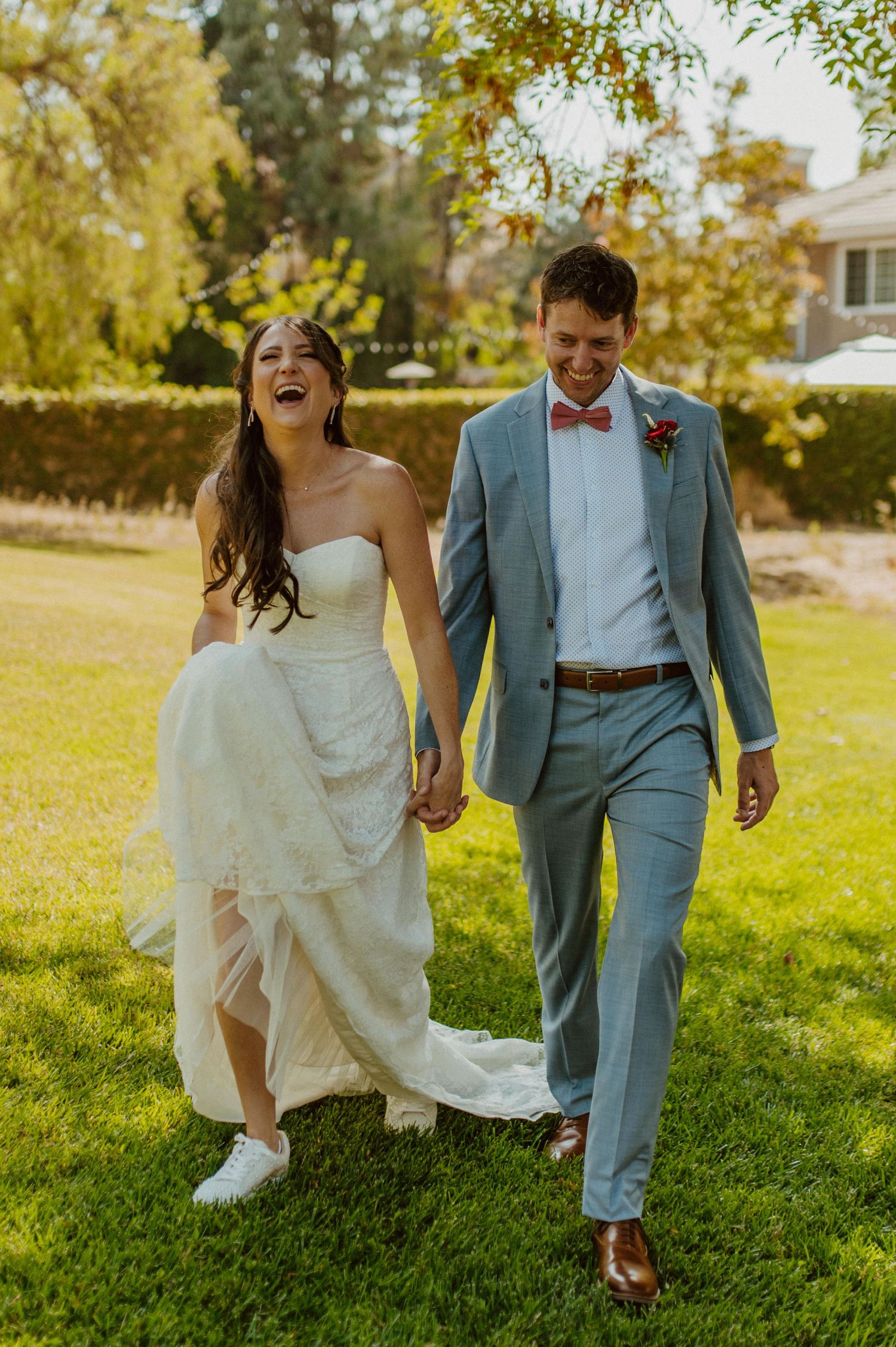 A couple runs playfully across a sunny lawn, the bride's dress flowing in the breeze.