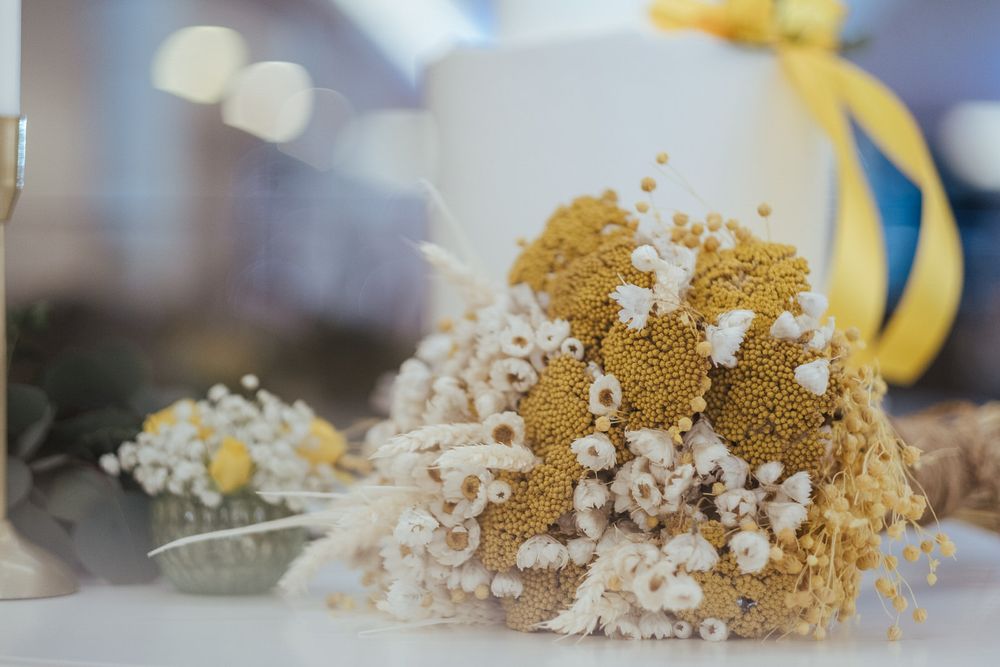 Flores de gypsophila secas com detalhes dourados e fita amarela criam um arranjo floral elegante.