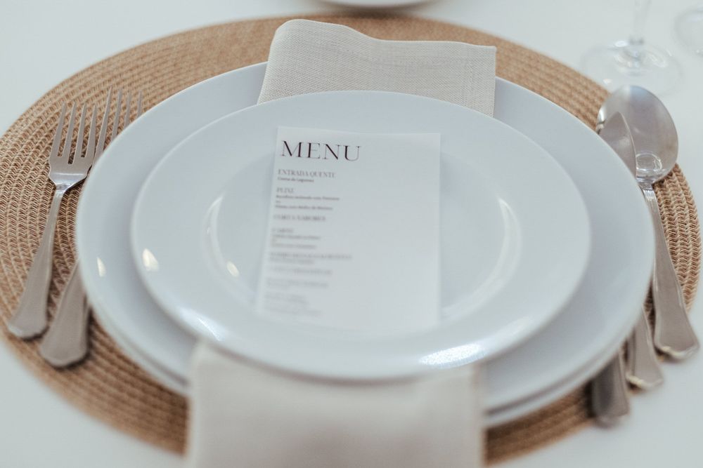 Mesa elegantemente posta com pratos brancos e menu sobre um individual de tecido.