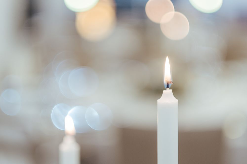 Uma única vela branca acesa com suaves luzes de efeito bokeh em segundo plano.