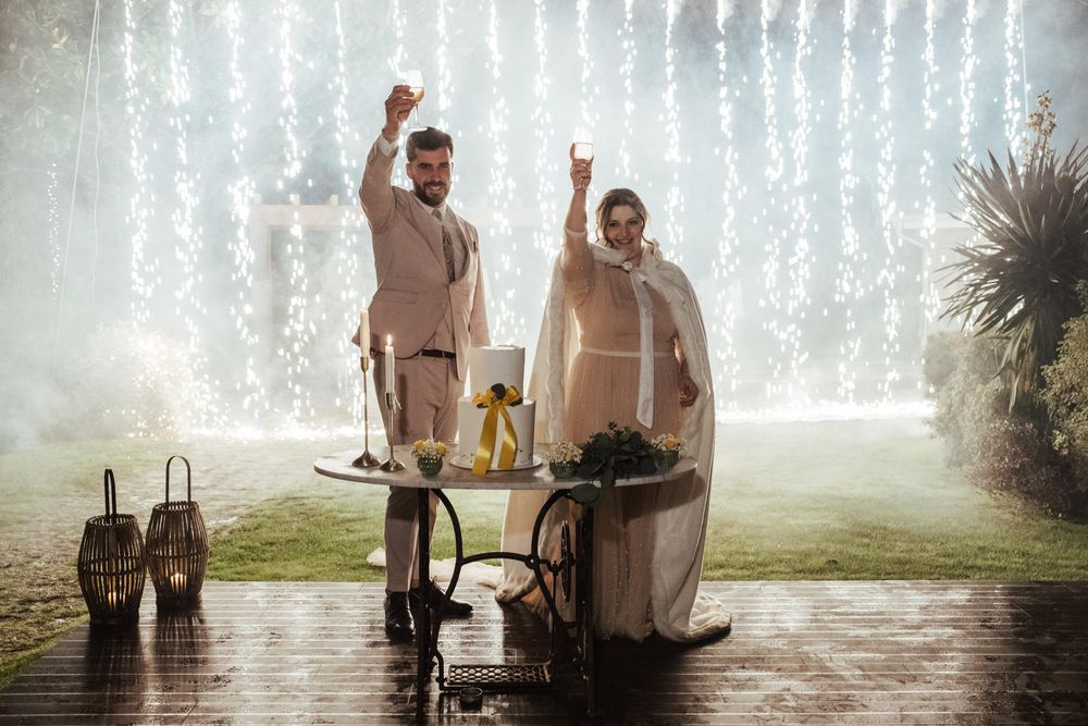 Casal a celebrar em frente a uma cortina de luzes em cascata num evento noturno ao ar livre.