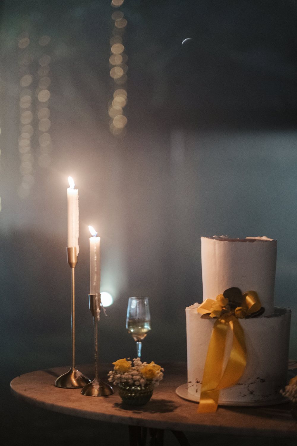 Elegante exposição de bolo de casamento com velas altas e fita dourada sob iluminação intimista.