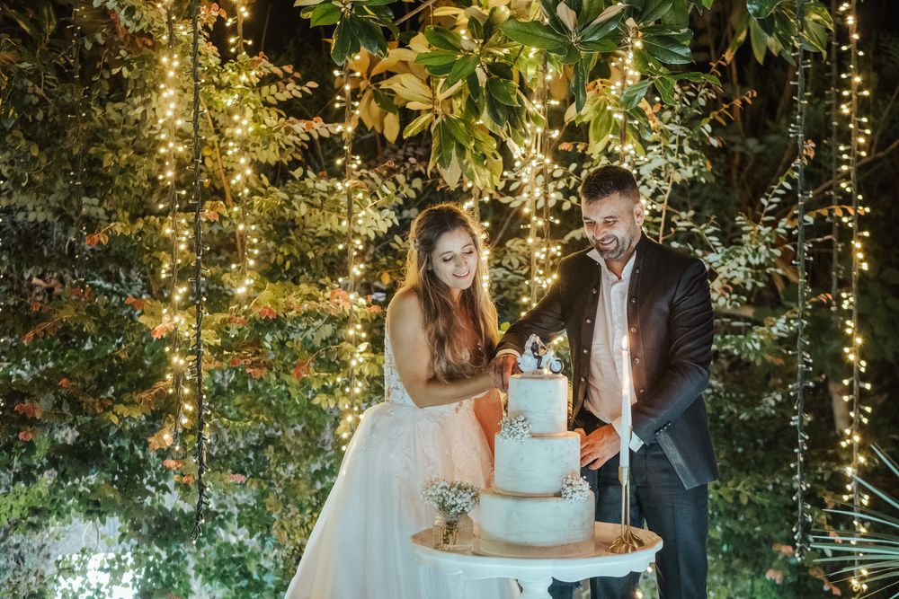 Cerimónia de corte do bolo de casamento sob luzes românticas e vegetação exuberante.