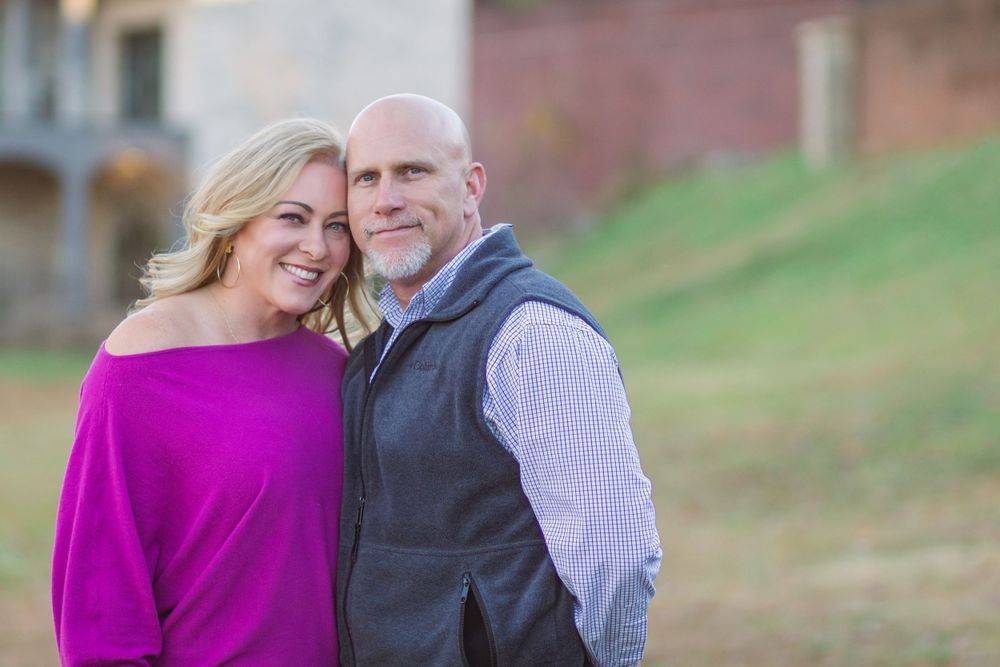 A couple in coordinating outfits embraces outdoors, with the woman wearing a vibrant magenta sweater.