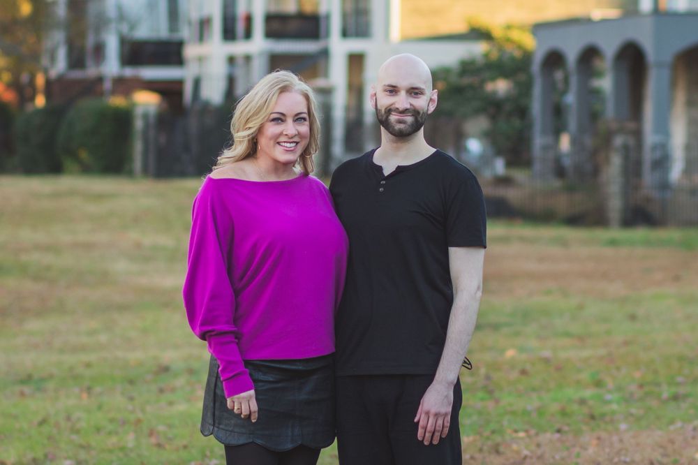 A couple poses outdoors, with one wearing a bright magenta top and the other in black.