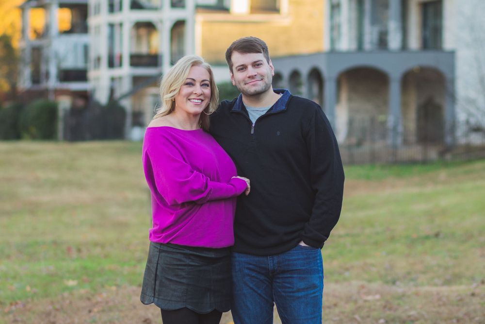 A pair poses casually outdoors against an apartment building backdrop in the late afternoon light.