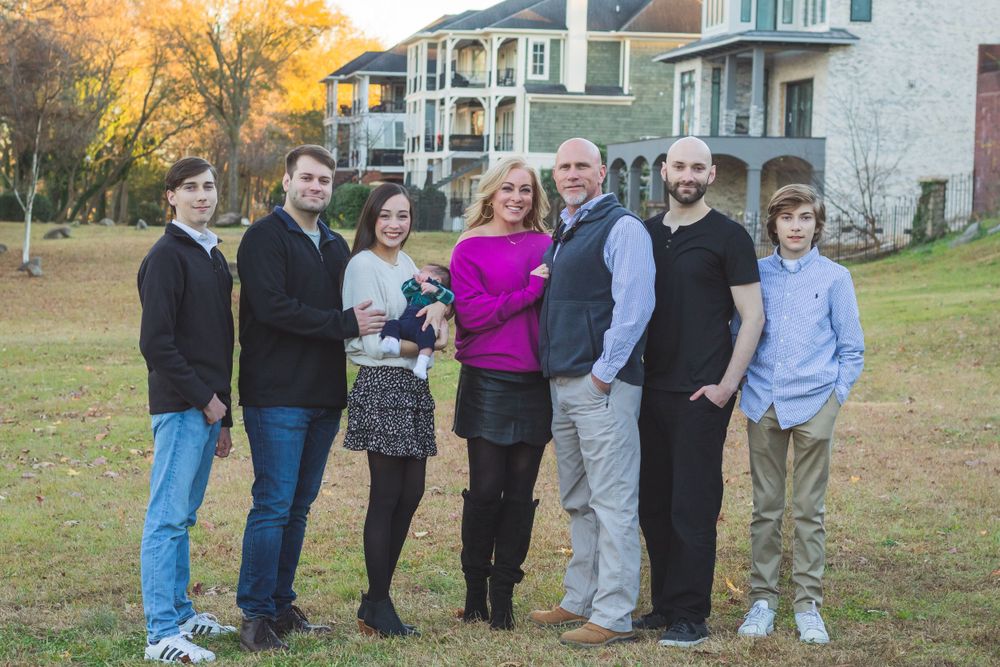Family group photo with eight people dressed casually standing on lawn with houses in background.