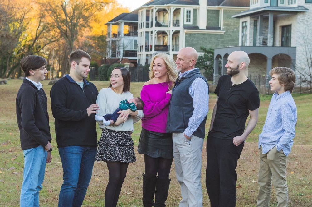 Extended family gathering outdoors in front of multi-story homes at sunset.