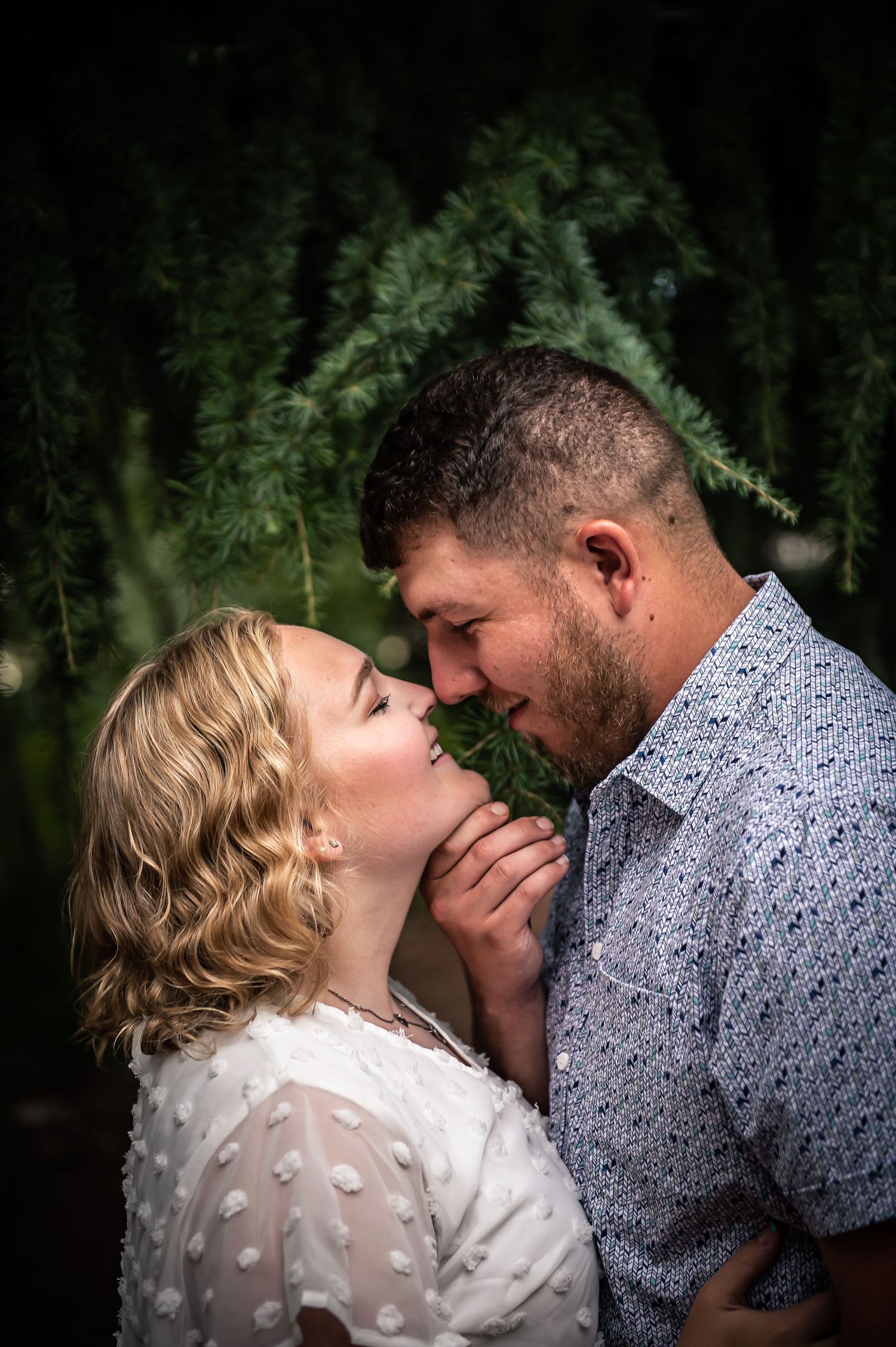 Intimate romantic portrait against dark green foliage background.