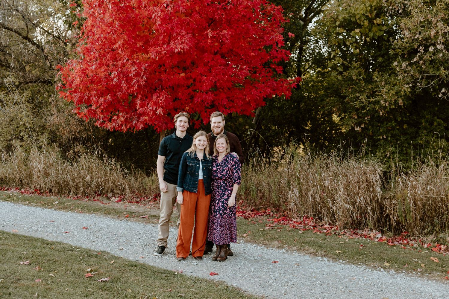 A group poses together in front of a brilliant red maple tree on an autumn day.